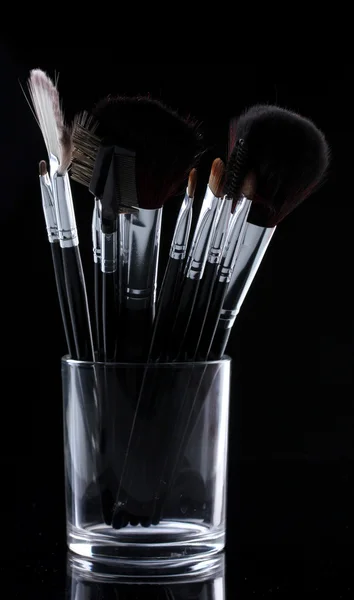 Make-up brushes in glass cup on black background — Stock Photo, Image