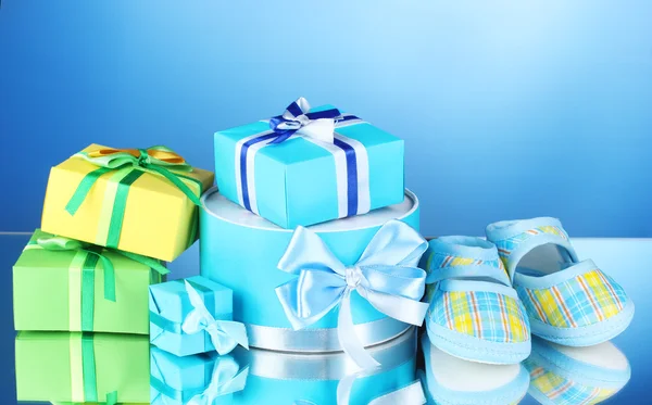 Beautiful gifts and babys bootees on blue background — Stock Photo, Image
