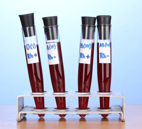 Tubes à essai avec sang sur table en bois sur fond bleu — Photo