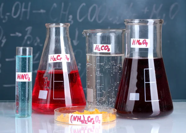 Пробирки с различными кислотами и другими химикатами на фоне доски — стоковое фото