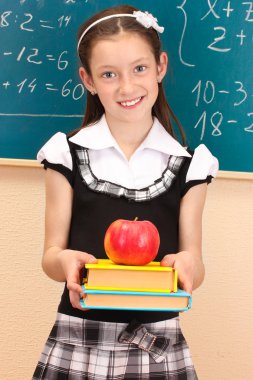 Beautiful little girl in school uniform with books and apple in class room clipart