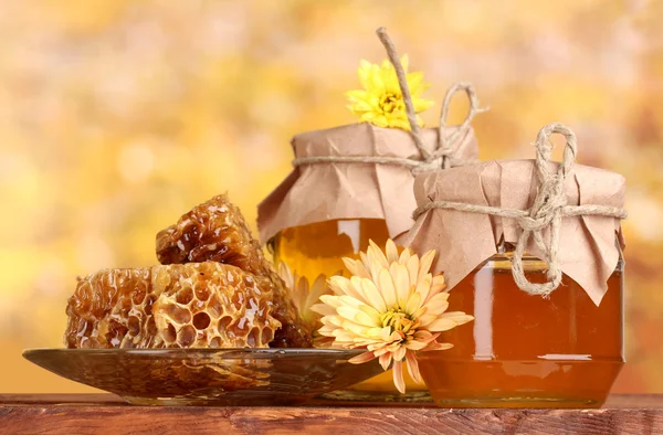 Due vasetti di miele, favi e drizzler in legno su tavola su fondo giallo — Foto Stock