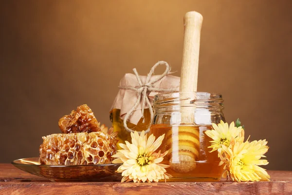 Dois frascos de mel, favos de mel e drizzler de madeira na mesa sobre fundo amarelo — Fotografia de Stock