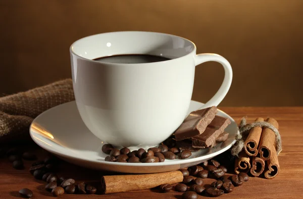 Cangkir kopi dan kacang-kacangan, tongkat kayu manis dan coklat di atas meja kayu di latar belakang coklat — Stok Foto