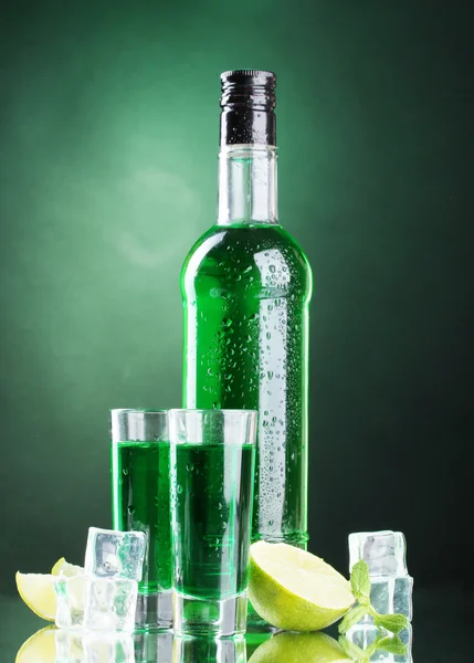 Флакон и стаканы абсента с лаймом и льдом на зеленом фоне — стоковое фото