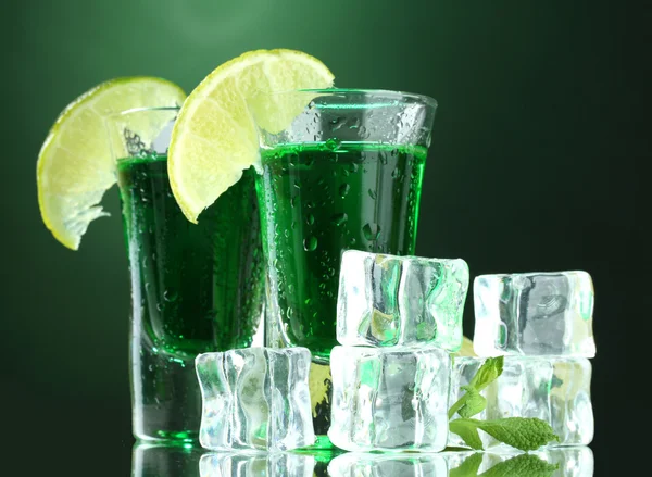 Dvě sklenice absintu, vápna a ledu na zeleném pozadí — Stock fotografie
