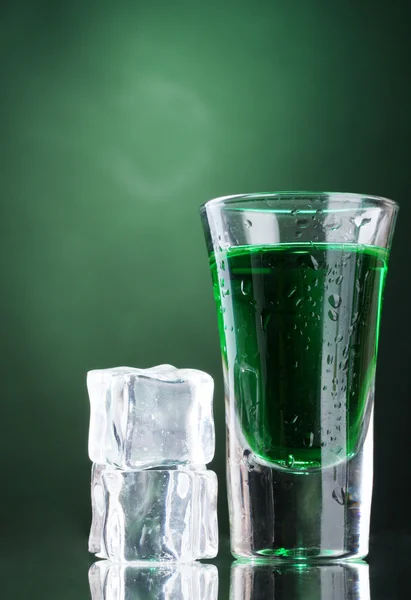 Glass of absinthe and ice on green background — Stock Photo, Image