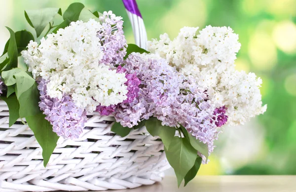 Mooie lila bloemen in mand op houten tafel op groene achtergrond — Stockfoto