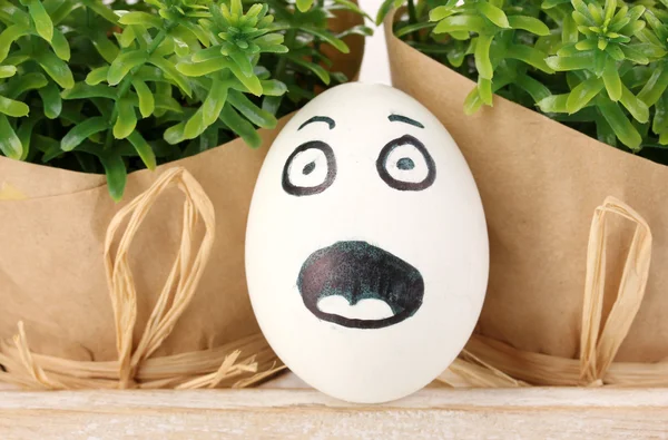 Белое яйцо со смешным лицом рядом с зелеными кустами — стоковое фото