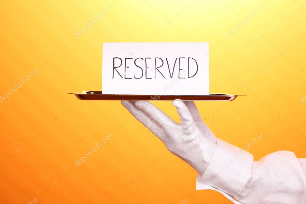 Hand in glove holding silver tray with card saying reserved on yellow background