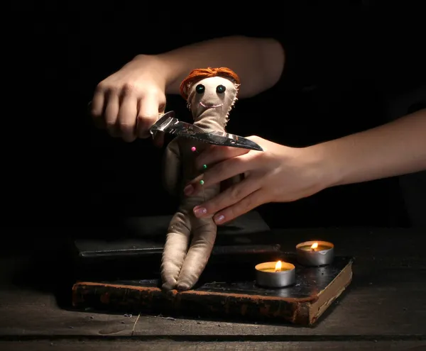 Кукла вуду, пронзённая ножом на деревянном столе при свете свечей — стоковое фото