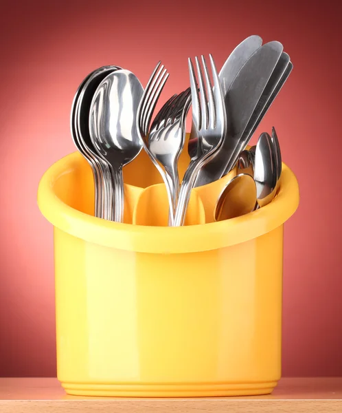 キッチン食器、ナイフ、フォークおよびスプーン黄色で赤い背景の上に立つ — ストック写真