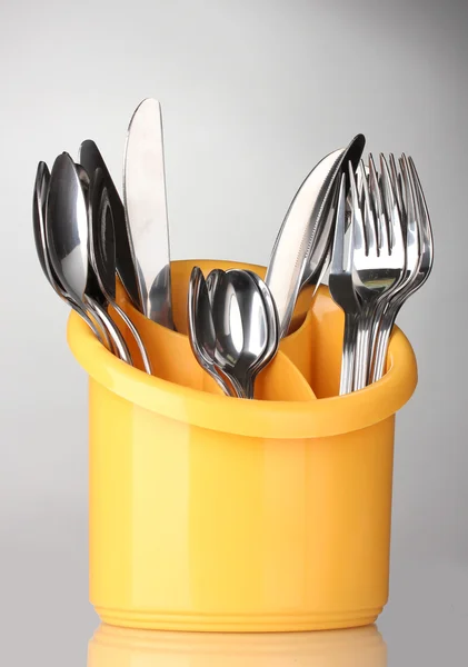 Keuken bestek, messen, vorken en lepels in geel staan op grijze achtergrond — Stockfoto