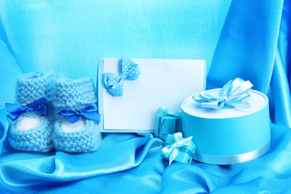Beaux cadeaux, babys bootees, carte postale vierge et mannequin sur soie bleue — Photo
