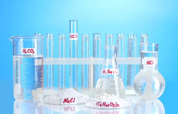 Tubos de ensaio com vários ácidos e produtos químicos sobre fundo azul — Fotografia de Stock