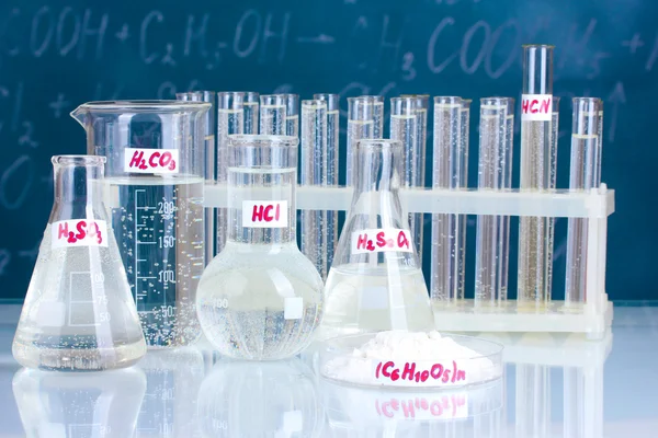 Zkumavky s různými kyselinami a dalších chemikálií na pozadí tabule — Stock fotografie