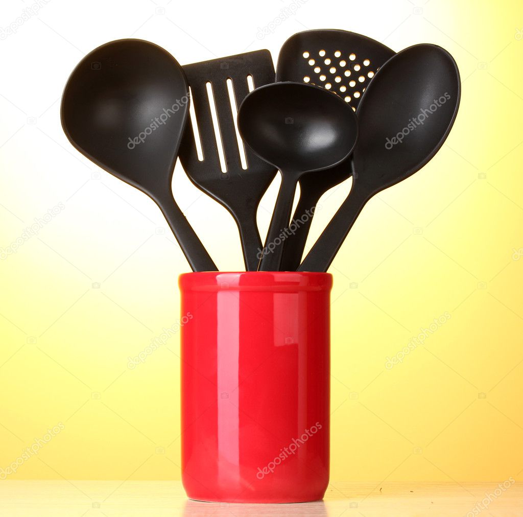 Black kitchen utensils in red cup on yellow background