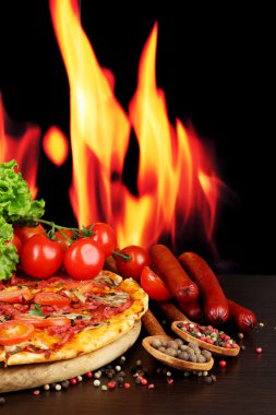 güzel pizza, salam, domates ve baharatlar alev arka plan üzerinde ahşap tablo