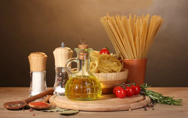 Spaghetti, tagliatelle in ciotola, vasetto di olio e verdure su tavola di legno su fondo marrone — Foto Stock
