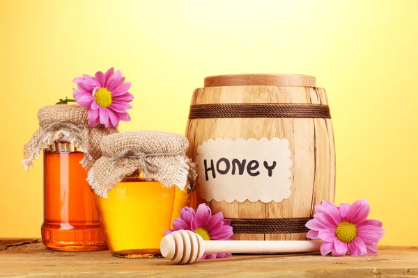 Miel dulce en barril y frascos con rociador sobre mesa de madera sobre fondo amarillo — Foto de Stock