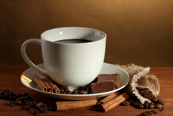 Kopje koffie en bonen, kaneelstokjes en chocolade op houten tafel op bruine achtergrond — Stockfoto