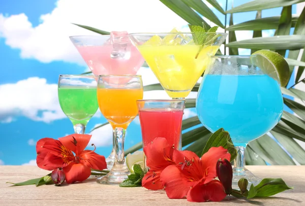 Екзотичні коктейлі та квіти на столі на фоні блакитного неба — стокове фото