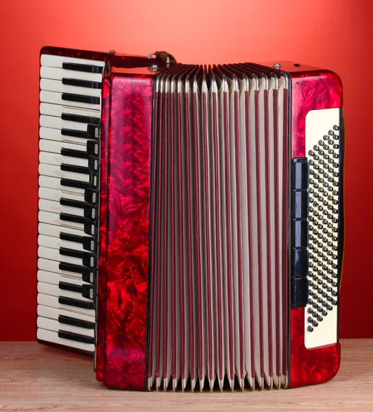Ретро аккордеон на деревянном столе на красном фоне — стоковое фото