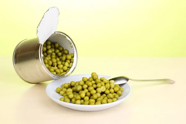 Offene Blechdose und Teller mit Erbsen und Löffel auf Holztisch auf grünem Hintergrund — Stockfoto