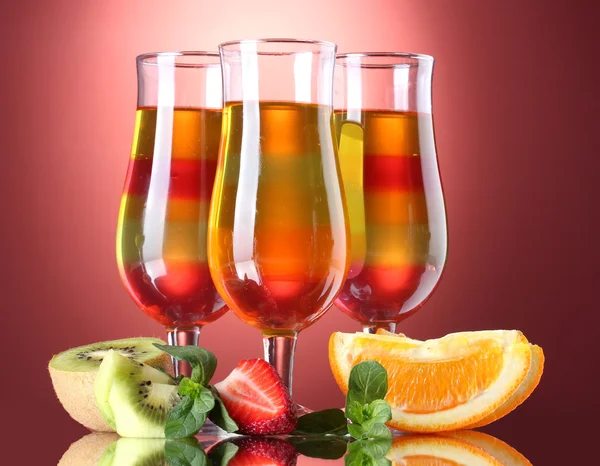 Fruit jelly in glasses and fruits on red background — Stock Photo, Image