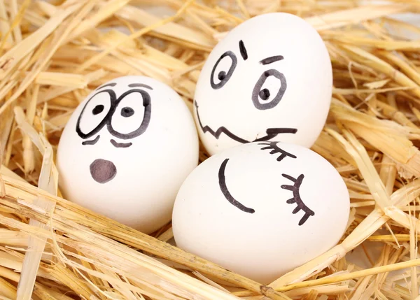 Ovos brancos com rostos engraçados em palha — Fotografia de Stock