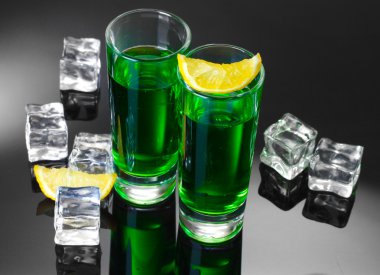 Two glasses of absinthe, lemon and ice on grey background clipart