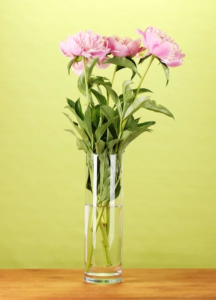 Three pink peonies in vase on wooden table on green background — Stock Photo, Image