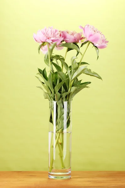 Drie roze pioenrozen in vaas op houten tafel op groene achtergrond — Stockfoto