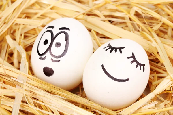 Ovos brancos com rostos engraçados em palha — Fotografia de Stock