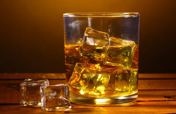 Glas Whiskey und Eis auf Holztisch auf braunem Hintergrund — Stockfoto
