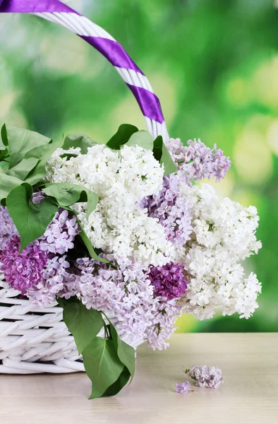 Bellissimi fiori lilla in cesto su tavolo di legno su sfondo verde — Foto Stock