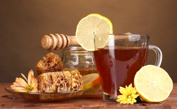 Honig, Zitrone, Waben und eine Tasse Tee auf einem Holztisch vor braunem Hintergrund — Stockfoto