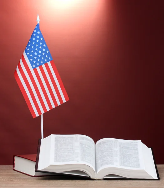 Bandiera americana sullo stand e libri su tavolo in legno su sfondo rosso — Foto Stock