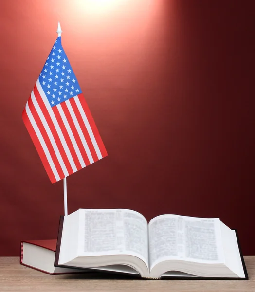 Bandeira americana no estande e livros sobre mesa de madeira no fundo vermelho — Fotografia de Stock