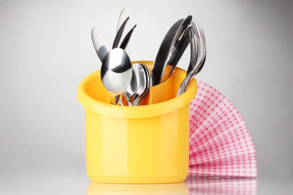 Kitchen cutlery, knives, forks and spoons in yellow stand with pink napkin on grey background — Stock Photo, Image