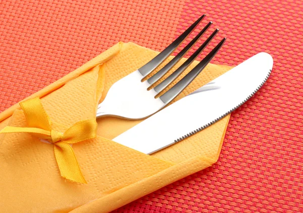Kırmızı masa örtüsü üzerinde yay ile sarı bir bez bıçak ve çatal — Stok fotoğraf