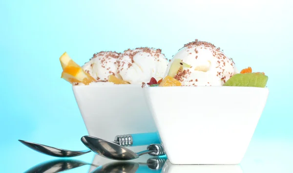 Вкусное ванильное мороженое с шоколадом и фруктами в мисках и ложках на синем фоне — стоковое фото
