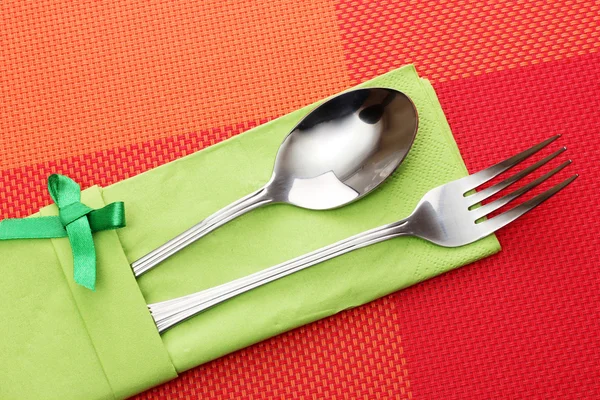 Πιρούνι και κουτάλι σε ένα πράσινο ύφασμα με πλώρη για ένα κόκκινο τραπεζομάντιλο — Φωτογραφία Αρχείου