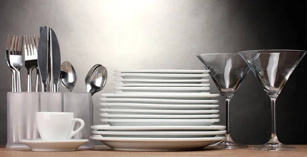 Assiettes, verres, gobelets et couverts propres sur table en bois sur fond gris — Photo