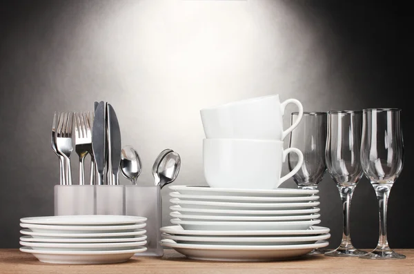 Clean plates, glasses, cups and cutlery on wooden table on grey background — Stock Photo, Image