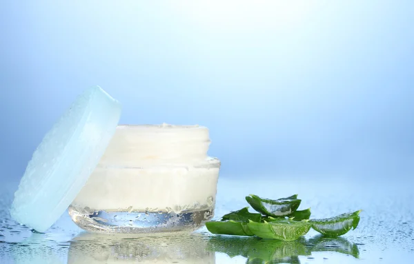 Frasco de vidro aberto de creme e aloés no fundo azul com gotas de água — Fotografia de Stock