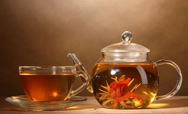 Théière en verre et tasse avec thé vert exotique sur table en bois sur fond brun — Photo