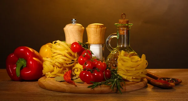 Локшина в мисці, банку з олією, спеціями та овочами на дерев'яному столі на коричневому фоні — стокове фото