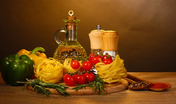 Nudlar i skål, burk med olja, kryddor och grönsaker på träbord på brun bakgrund — Stockfoto