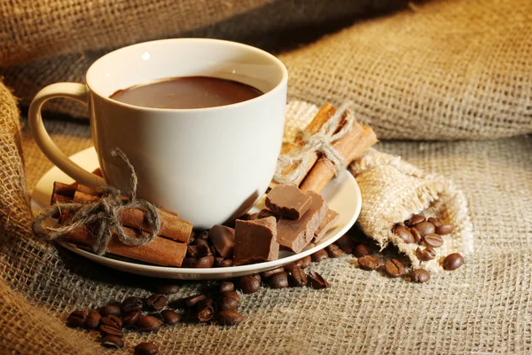 Csésze kávé és a bab, a fahéjat és a csokoládé a háttérben zsákolás — Stock Fotó